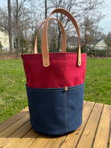 Tall Large Red & Blue heavy-duty canvas garden tool bag with four deep exterior pockets holding seed packets. Features durable Leather handles and a structured round base for upright utility.