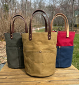 Three Large Olive Green, Tan and Red & Blue heavy-duty canvas garden tool bag with four deep exterior pockets holding seed packets. Features durable webbing grab handles and a structured round base for upright utility.