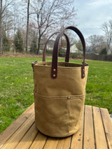 Tall Large Hybrid Waxed Canvas in Tan garden tool bag with four deep exterior pockets holding seed packets. Features durable Leather handles and a structured round base for upright utility.