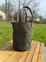 Tall Large Olive Green heavy-duty canvas garden tool bag with four deep exterior pockets holding seed packets. Features durable Leather handles and a structured round base for upright utility.