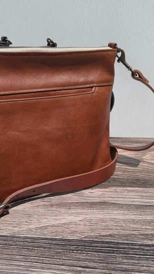 Video of a Group photo showcasing four handcrafted Leather Bayside Crossbody bags, each made with Horween leather in unique finishes. Bags are arranged to show variations in leather color and grain—Sienna, Vintage Dark Brown, Bomber Jacket Black, and Rustic Charcoal—each featuring solid brass hardware, a full metal zipper, and an adjustable vegetable-tanned leather strap. Designed and made in Maryland.